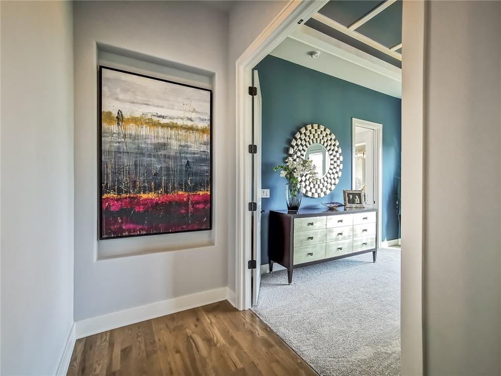 Entry hallway with wood flooring and framed art, opening to a furnished room with a teal accent wall.