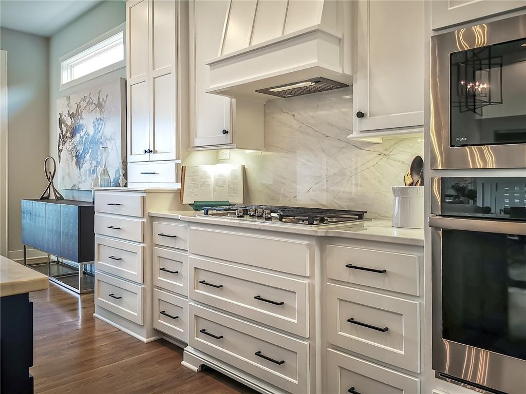 Bright kitchen with white cabinetry, marble backsplash, gas cooktop, and stainless steel double ovens.