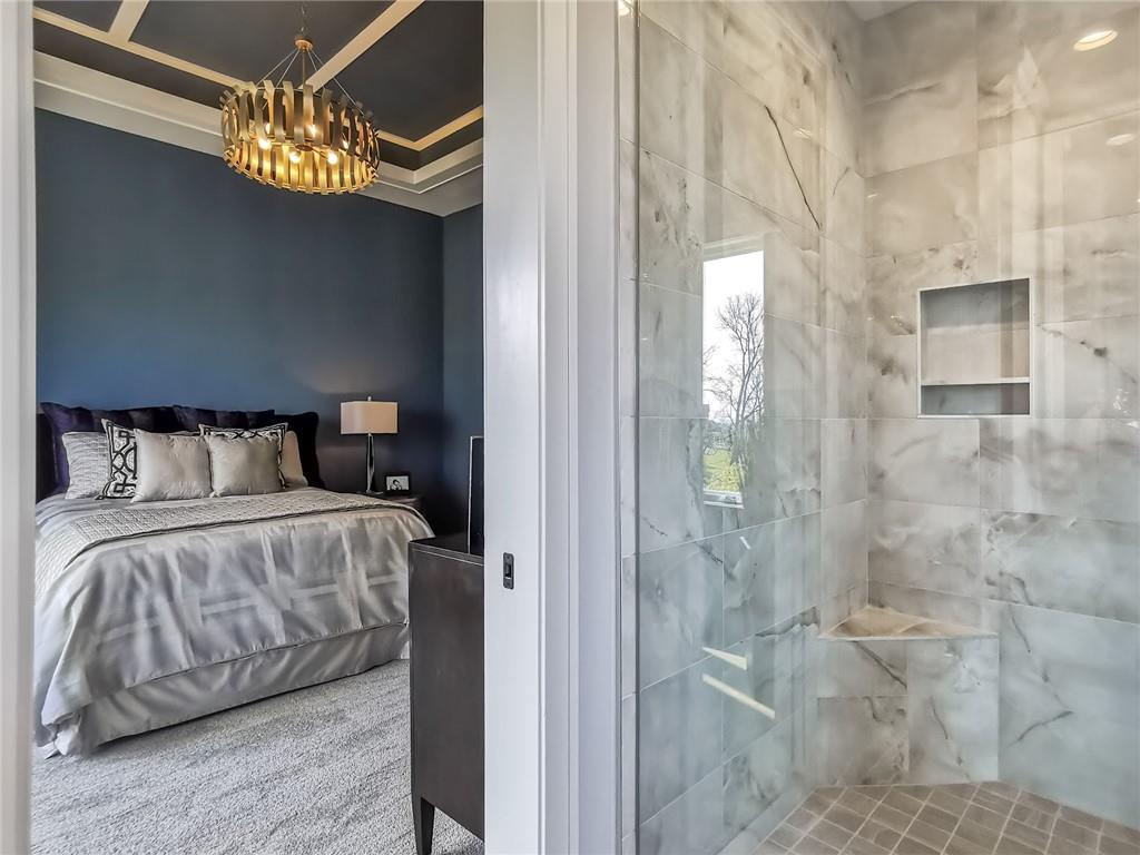Bedroom with a dark accent wall and chandelier beside a marble-tiled walk-in shower.