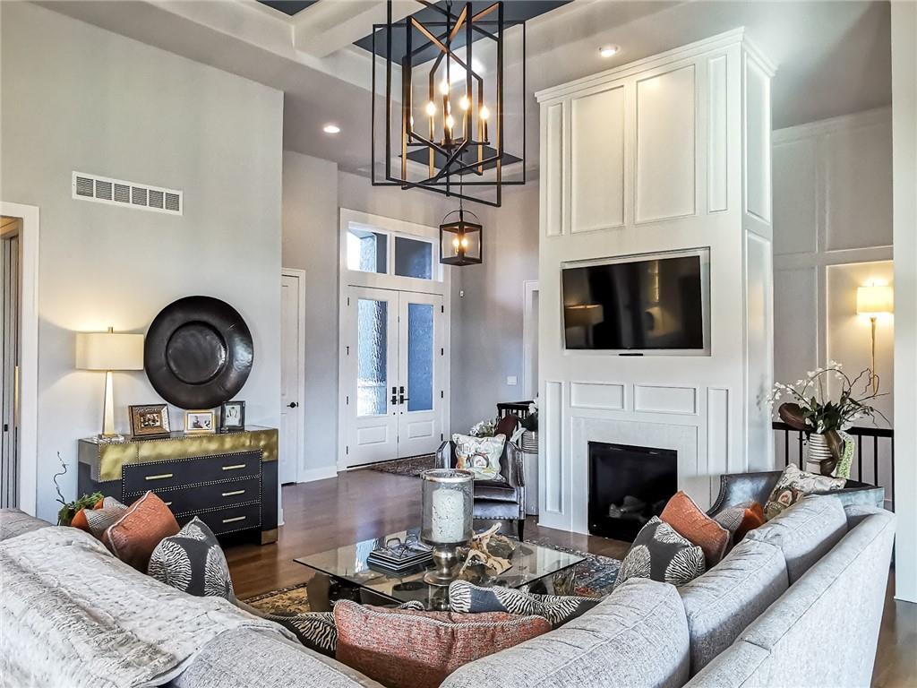 Staged living room with a tall fireplace wall, mounted television, and double-height entry.