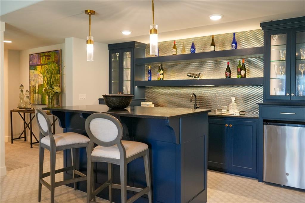 Wet bar with navy cabinetry, illuminated bottle shelves, and a raised counter with stools.
