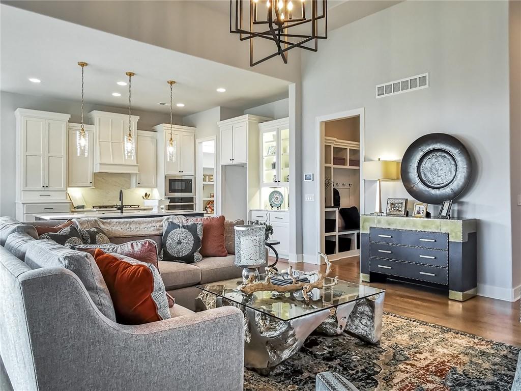 Open living room and kitchen with a gray sectional, white cabinetry, and a glass coffee table.