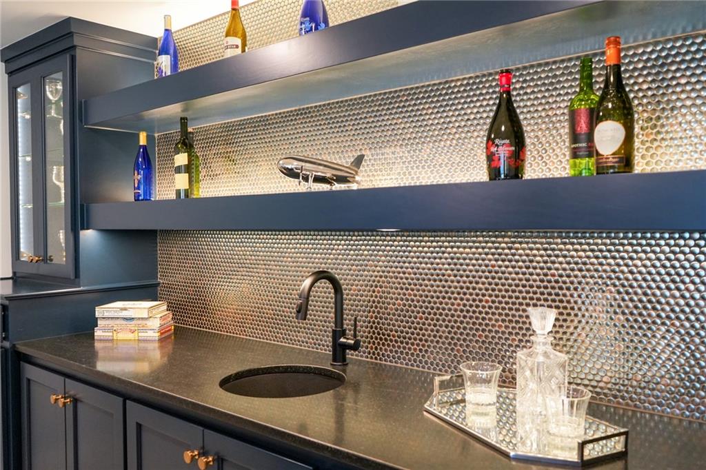 Wet bar with a dark stone counter, metallic backsplash, display shelves, and glassware.