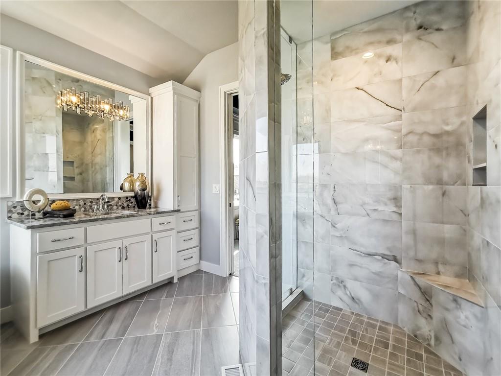 Bathroom with a marble-tiled glass shower and white double vanity.
