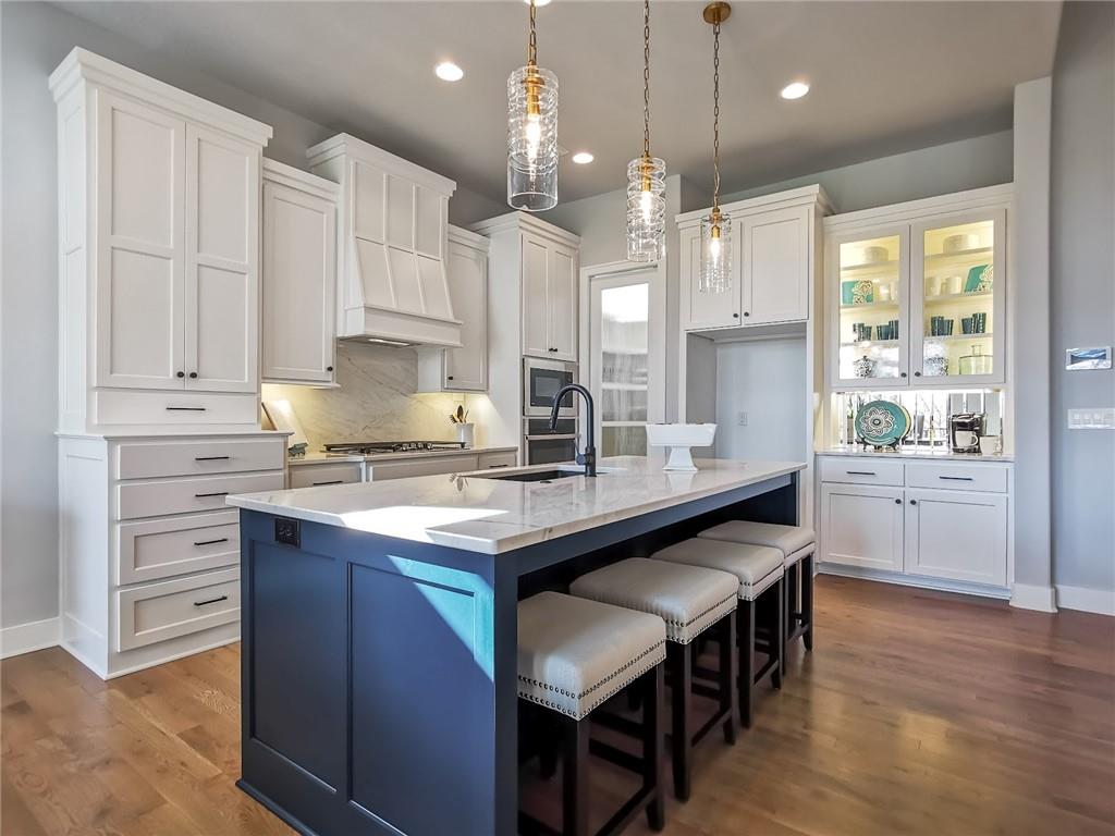 Kitchen with white cabinetry, a blue island, marble counters, and three upholstered stools.