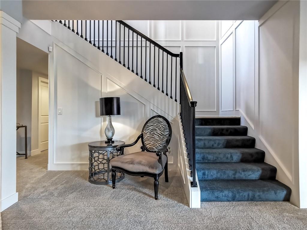 Entry foyer with a carpeted staircase, black railing, and upholstered accent chair.