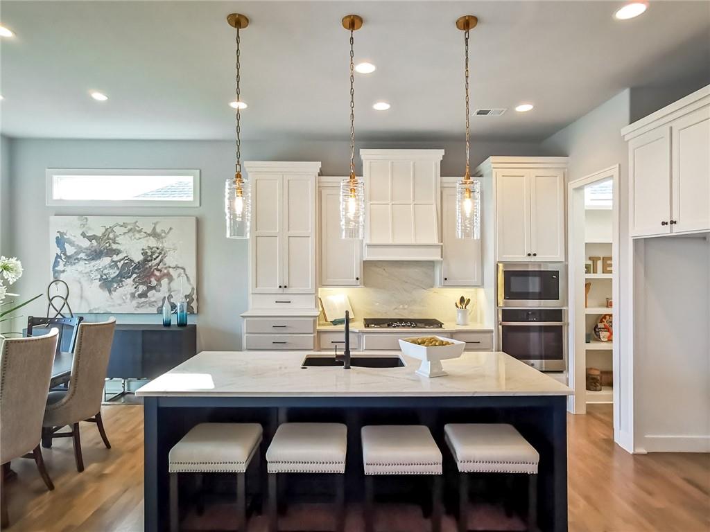 Kitchen with a large island, white cabinetry, pendant lights, and four bar stools.