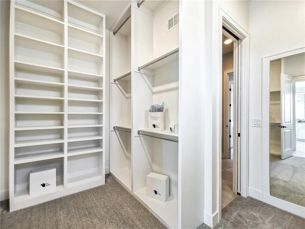 Walk-in closet with built-in shelving, hanging rods, and carpeted floor.