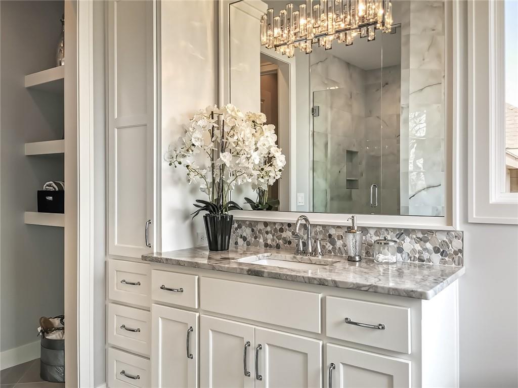 Bathroom vanity with marble counter, mosaic backsplash, and a glass-enclosed shower.