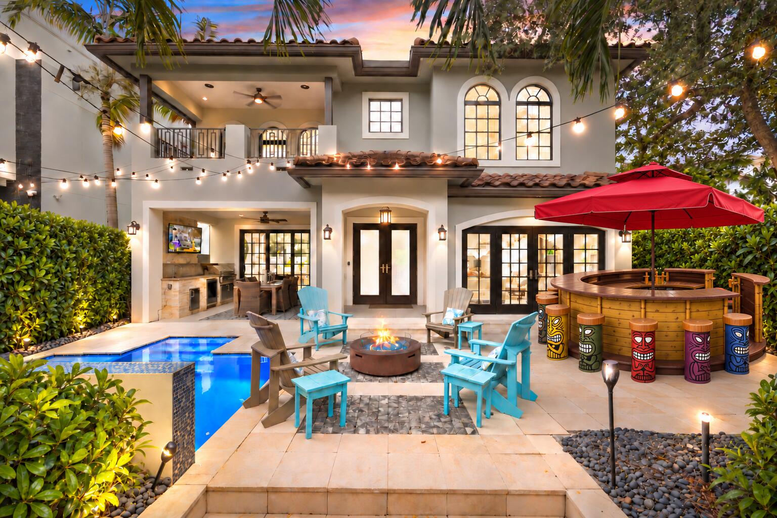 Backyard with a pool, outdoor kitchen, fire pit seating, and colorful tiki bar at dusk.