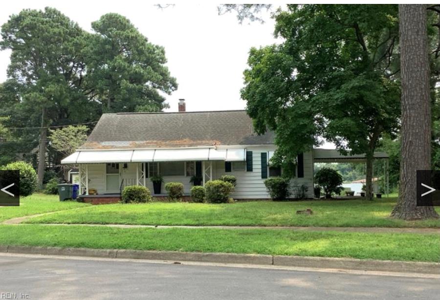 Single-story white house with a broad porch, right-side carport, and mature trees.