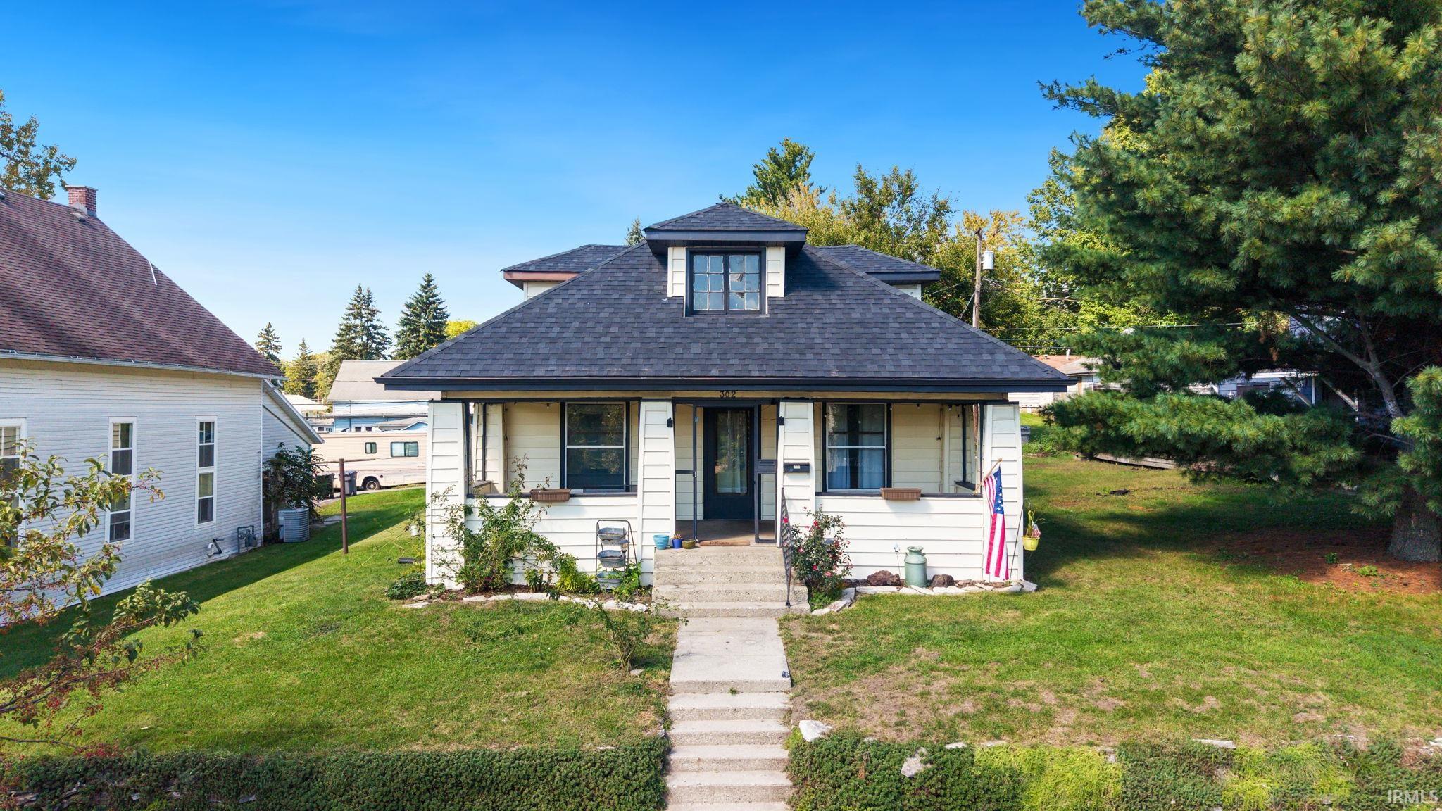 White house with a broad hipped roof, covered porch, front walkway, and American flag.