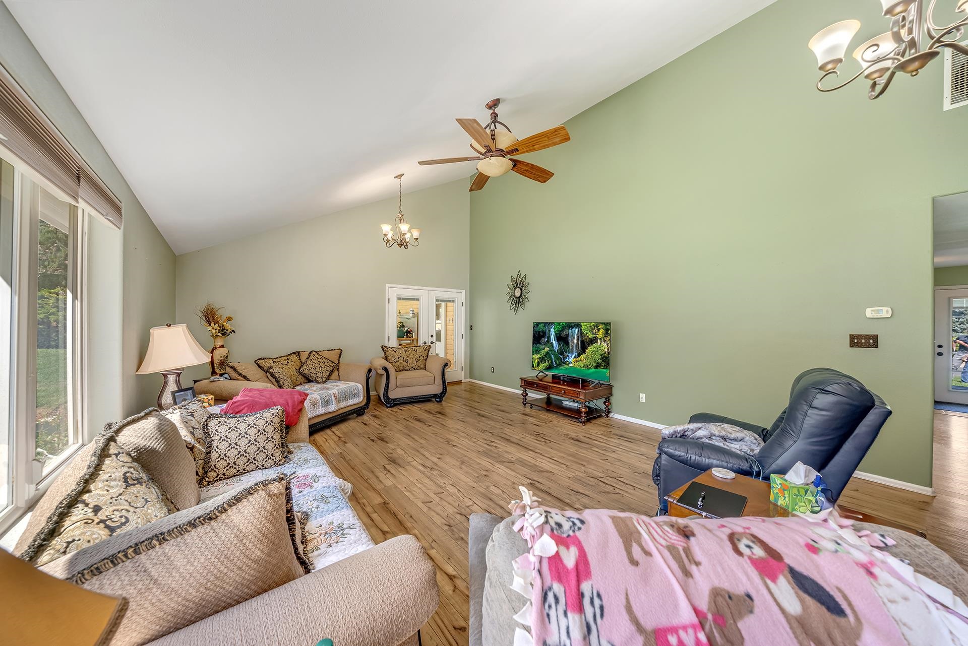 Furnished living room with a vaulted ceiling, wood-look floors, large windows, and multiple seating areas.