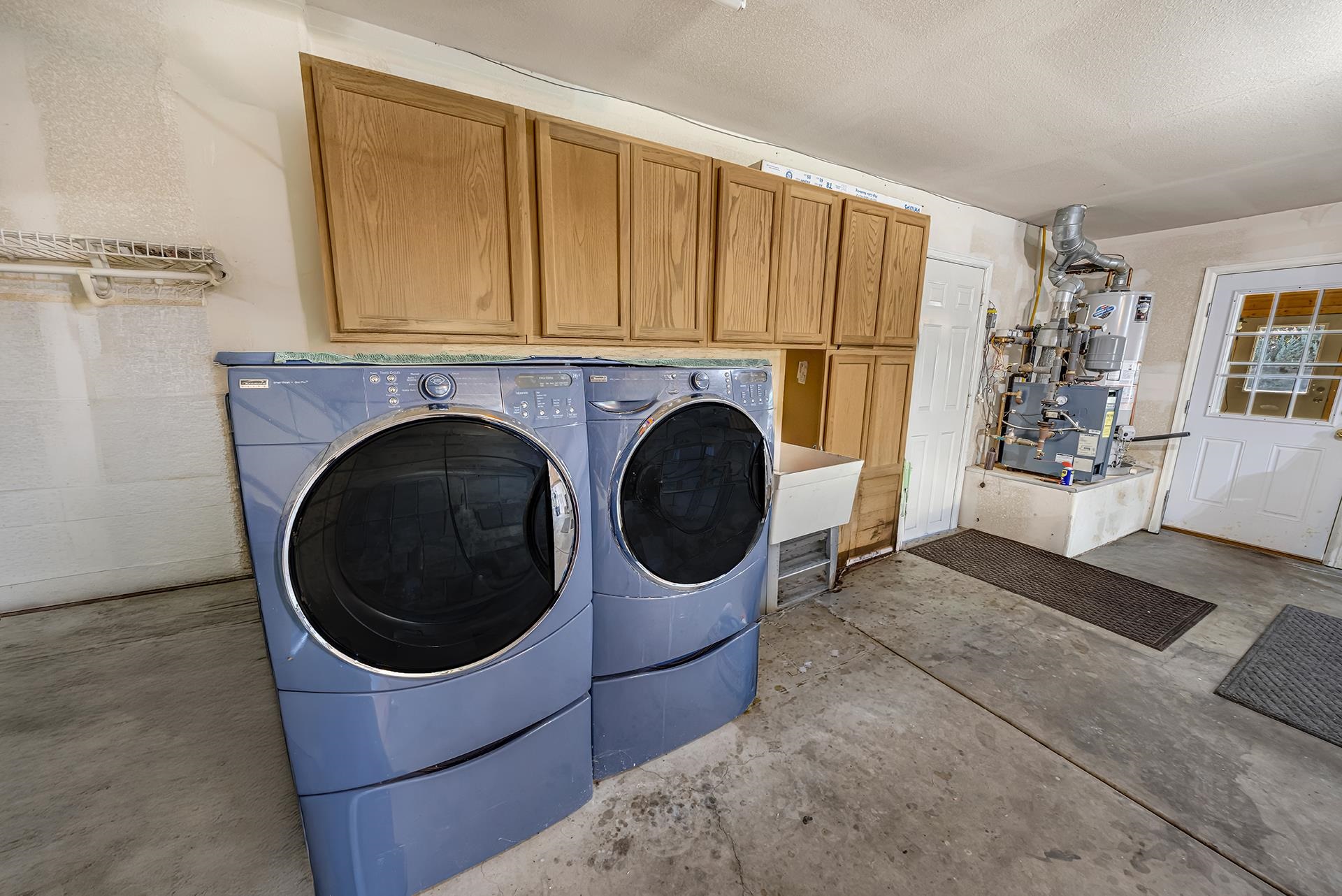 Garage laundry area with front-loading washer and dryer beneath oak cabinets.
