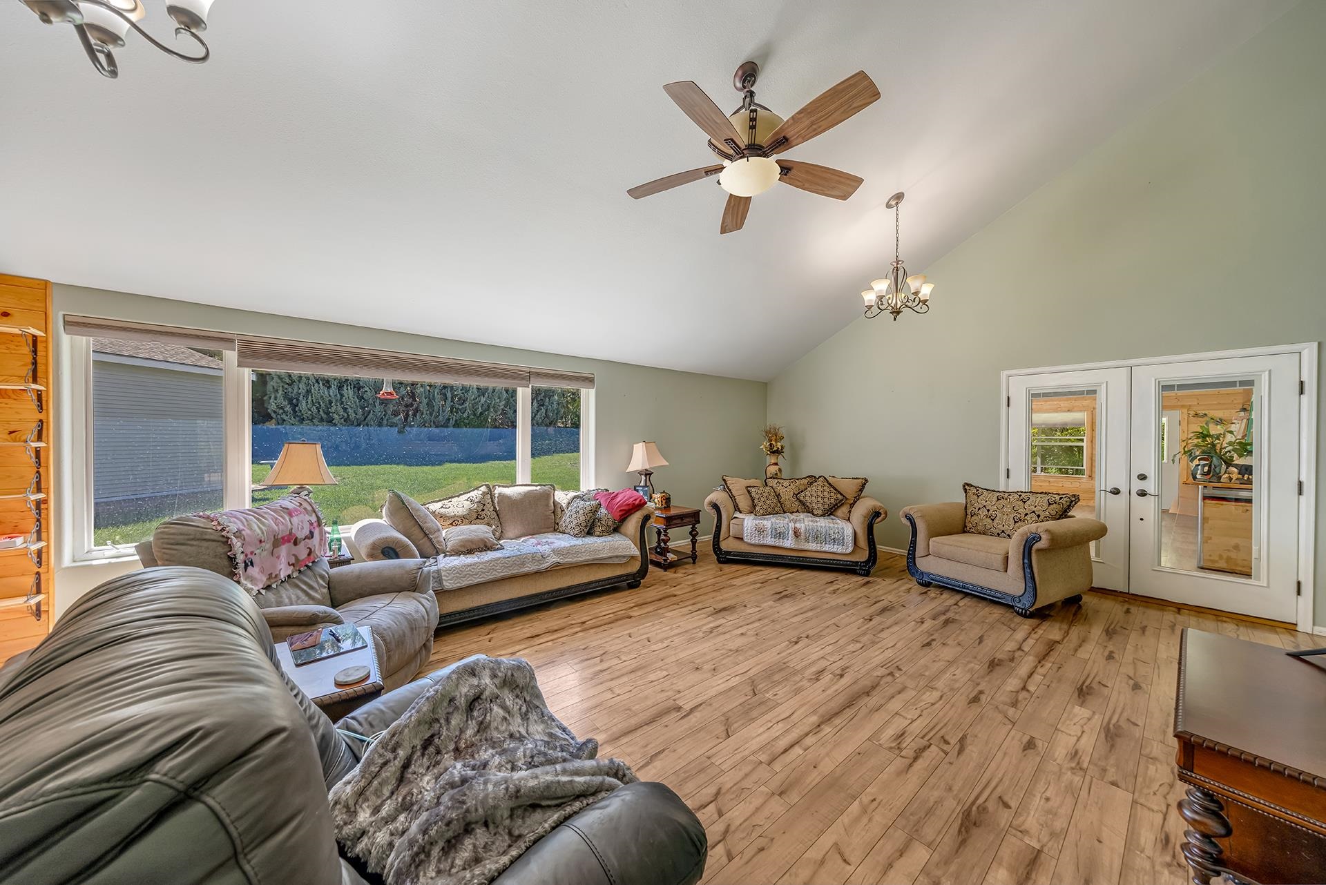 Furnished living room with wide windows, wood flooring, and a vaulted ceiling with ceiling fans.