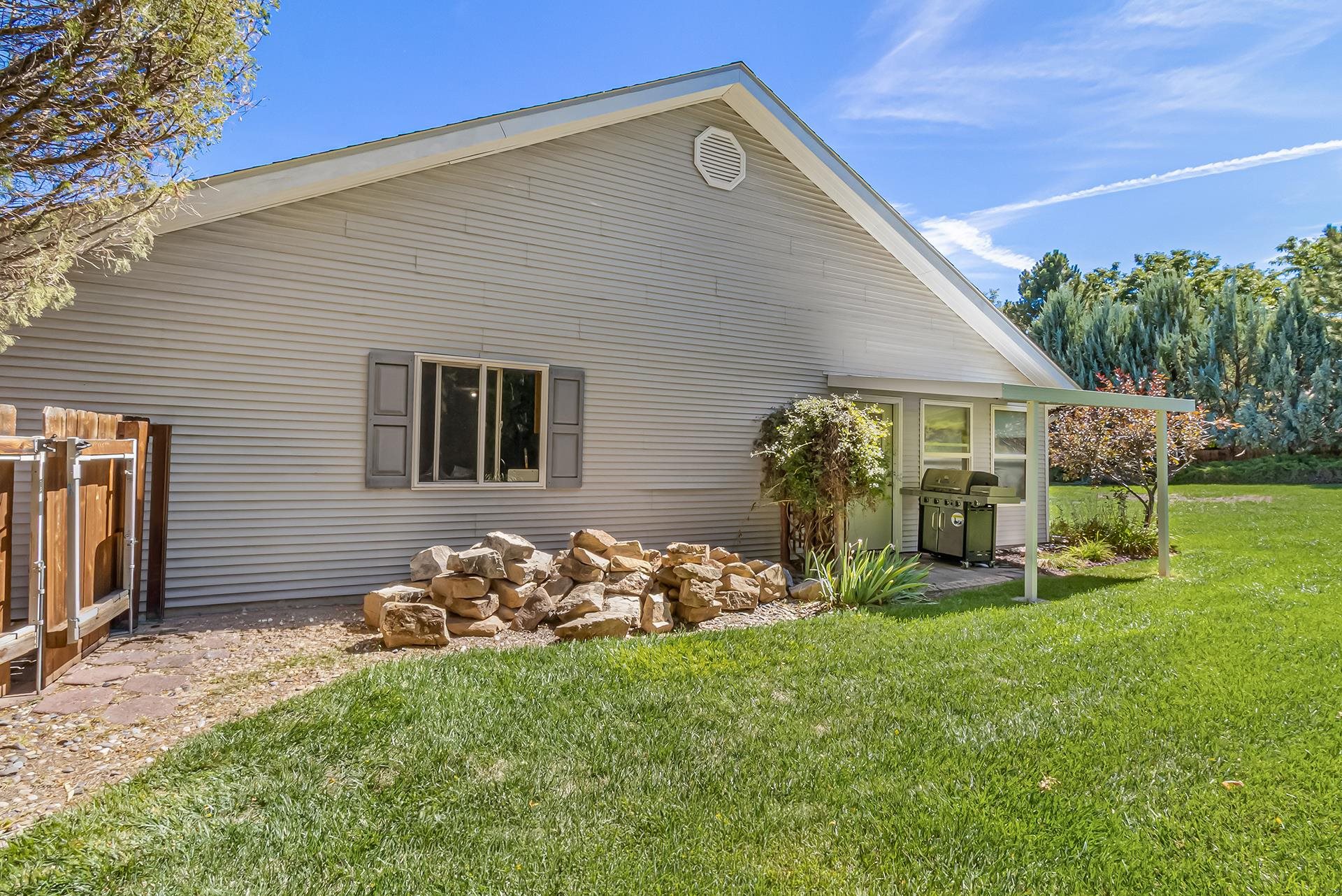 Rear of a gray-sided house with a covered patio, gas grill, and lawn.