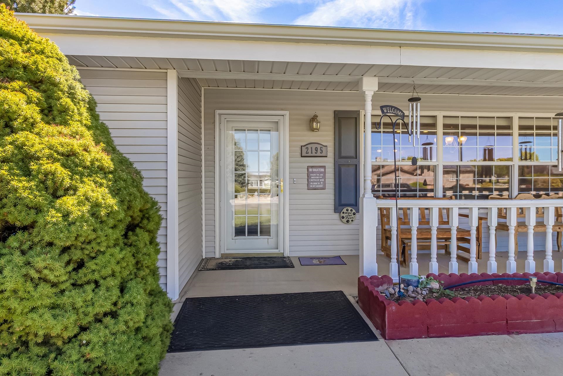 Home’s covered front porch with a glass entry door, white railing, and outdoor dining area.