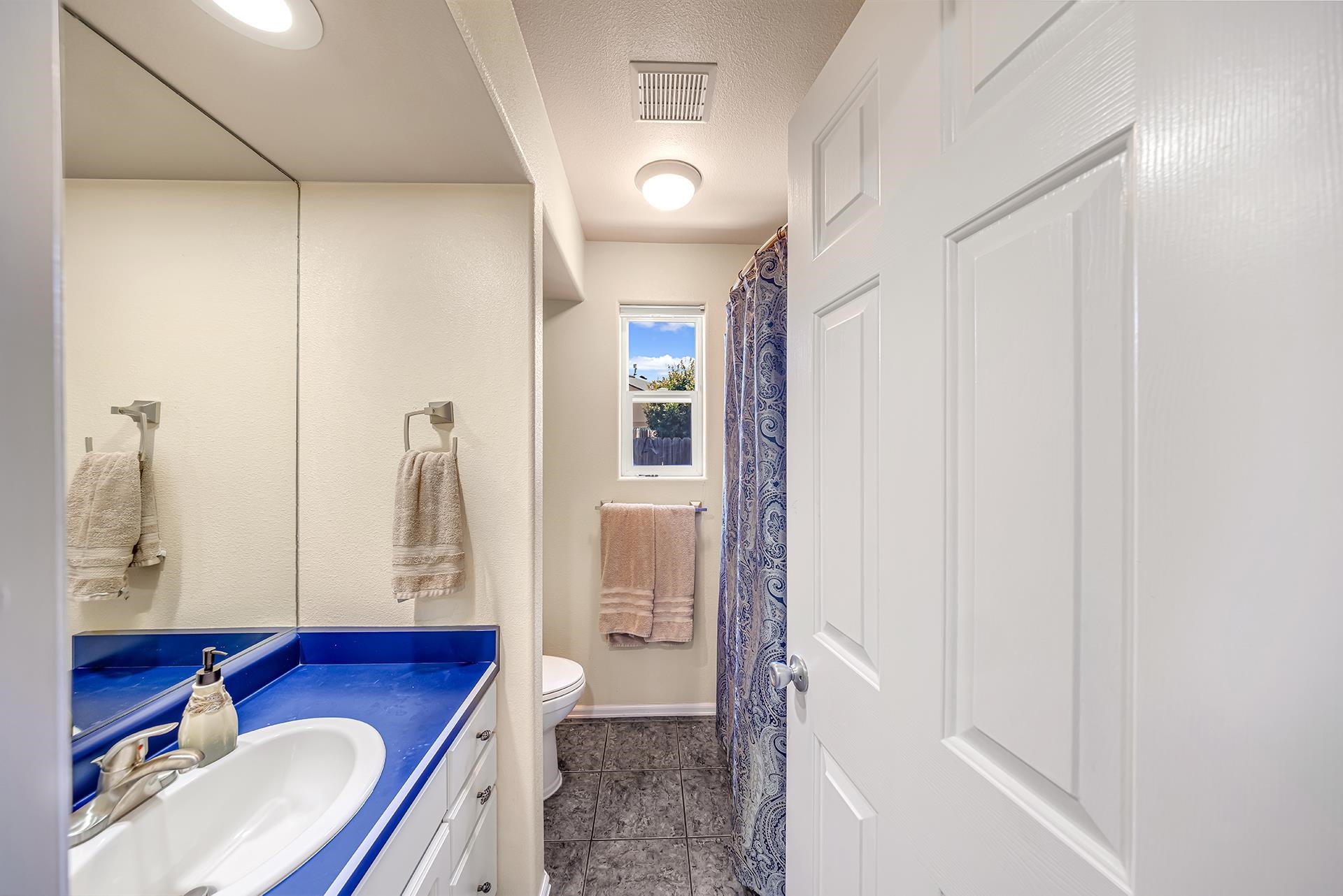 Bathroom with a bright blue vanity, large mirror, gray tile floor, and patterned shower curtain.