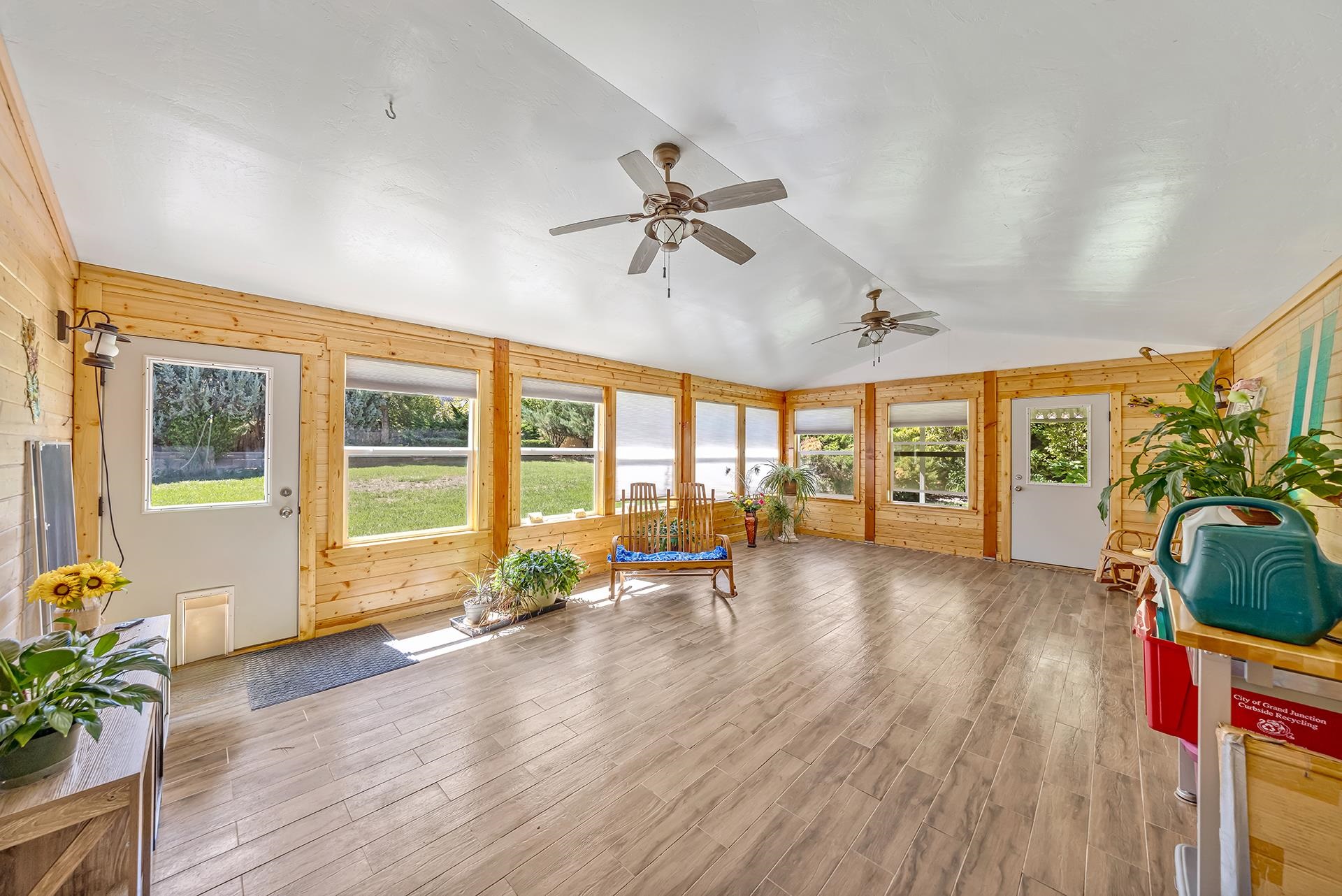 Bright sunroom with wood-paneled walls, large windows, ceiling fans, and a wooden bench.