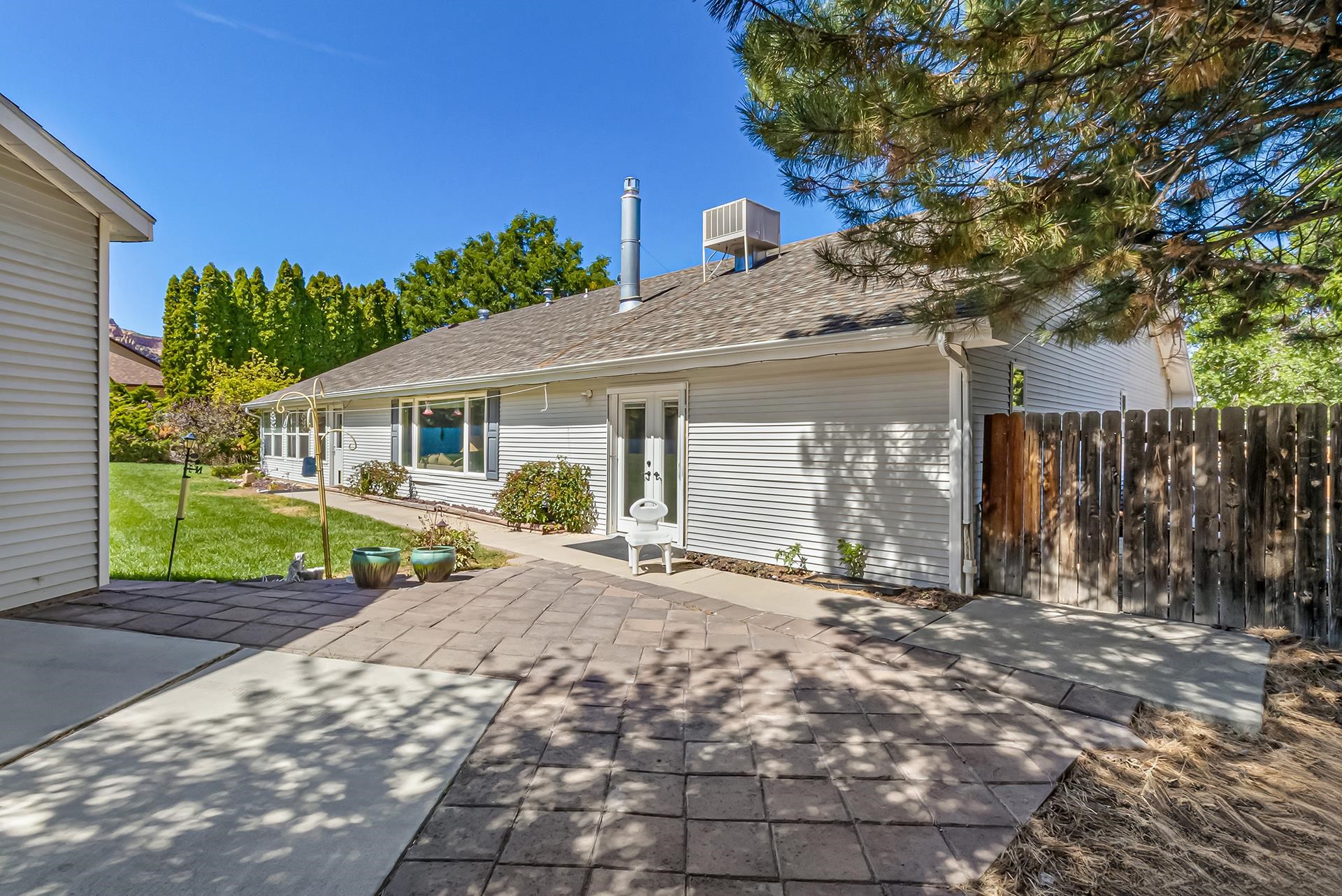 Single-story home with a paved backyard patio, lawn, and wooden fence.
