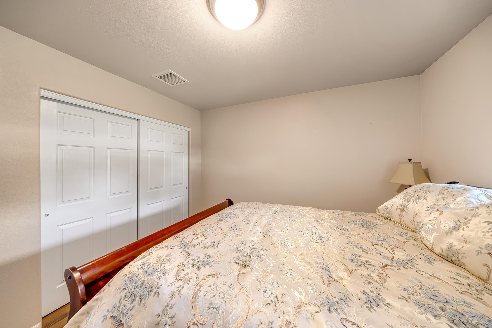 Furnished bedroom with floral bedding and white closet doors.
