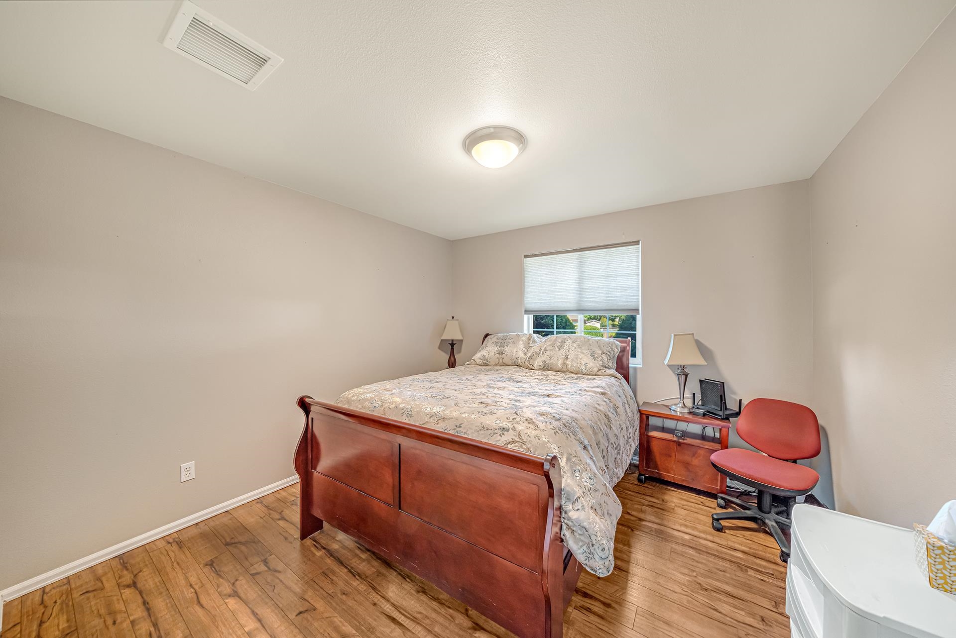 Bedroom with a wooden bed, patterned bedding, wood-look tile flooring, and a window with a lowered shade.