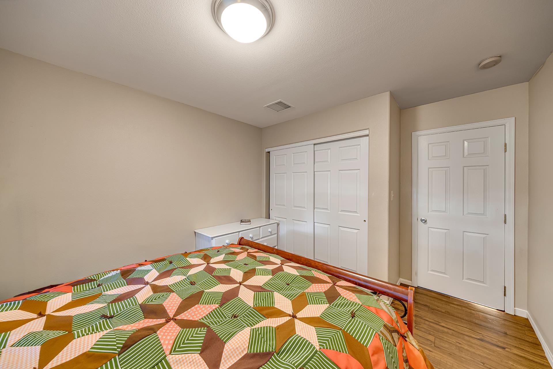 Bedroom with a colorful patchwork bedspread, white closet doors, and wood flooring.