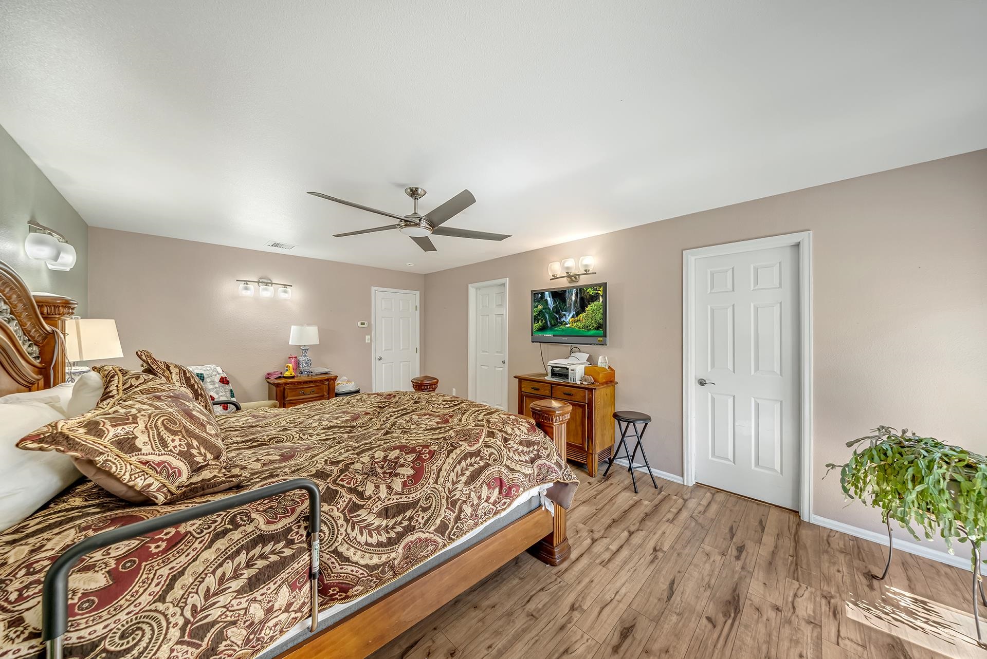 Furnished bedroom with an ornate patterned bedspread, ceiling fan, and wood-look flooring.