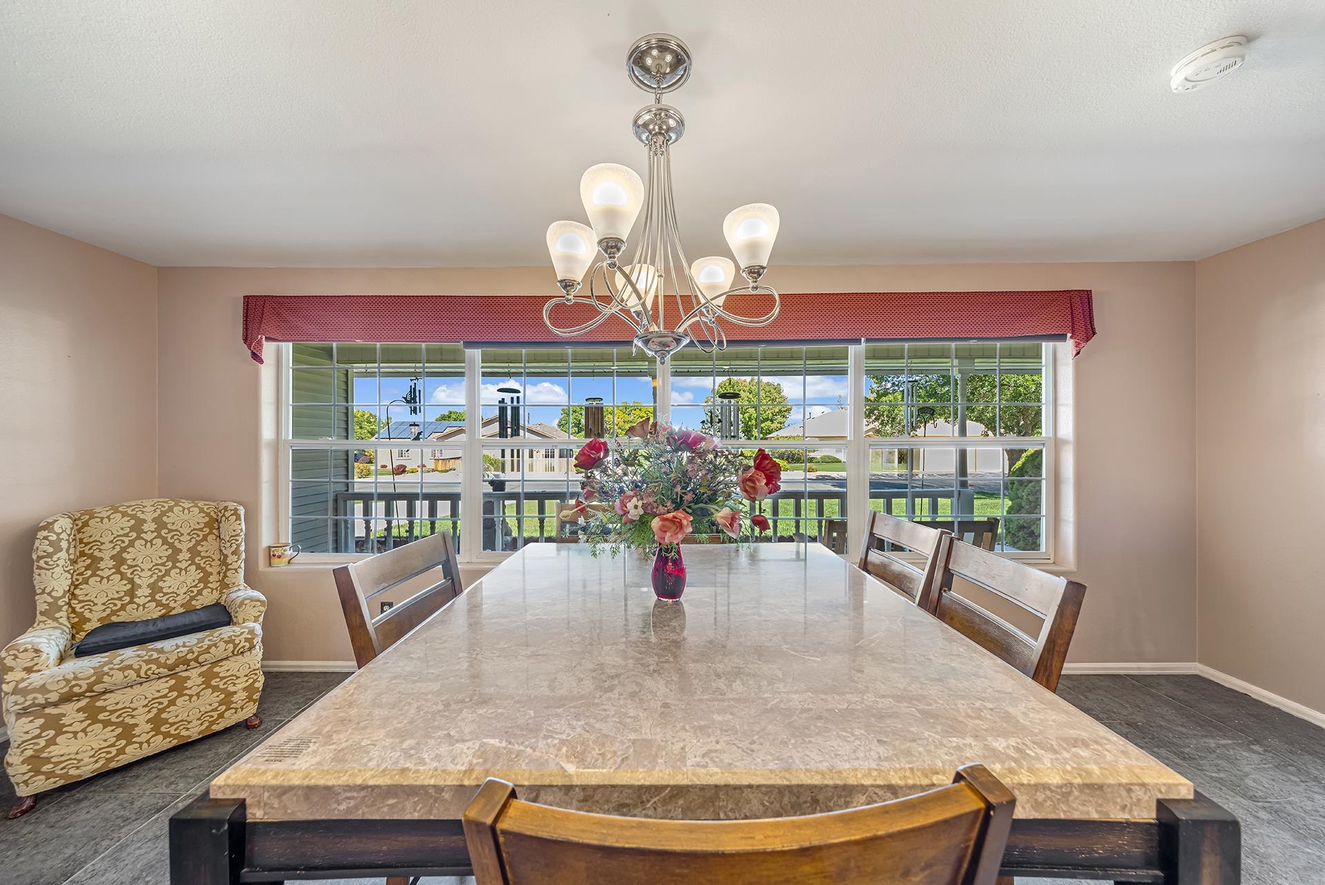 Dining room with a large table, chandelier, and wide windows overlooking the yard.