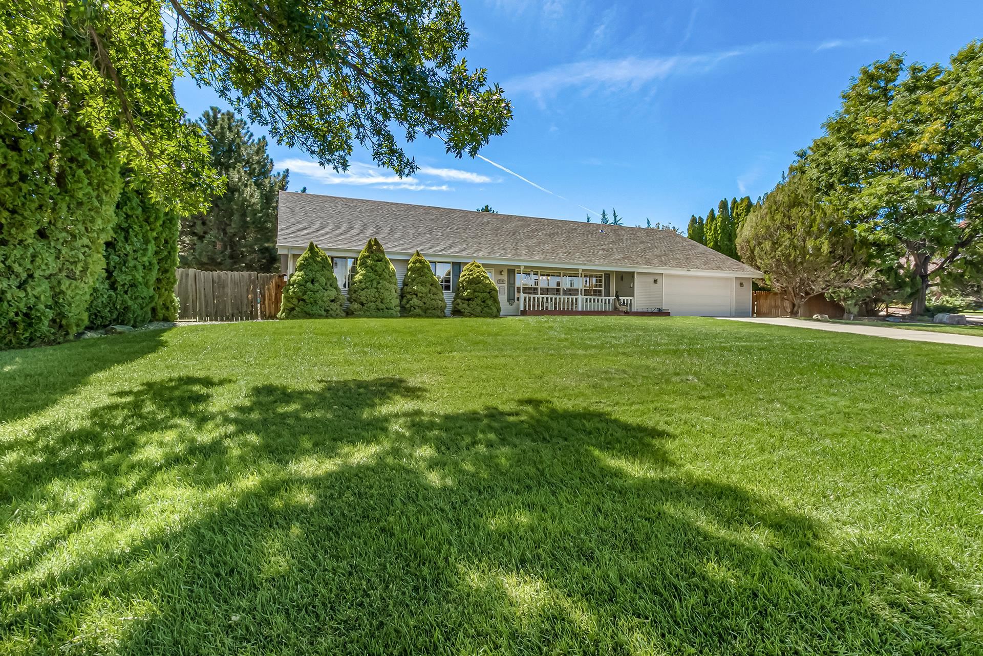 Single-story home with a covered porch and attached garage behind a broad, tree-shaded lawn.