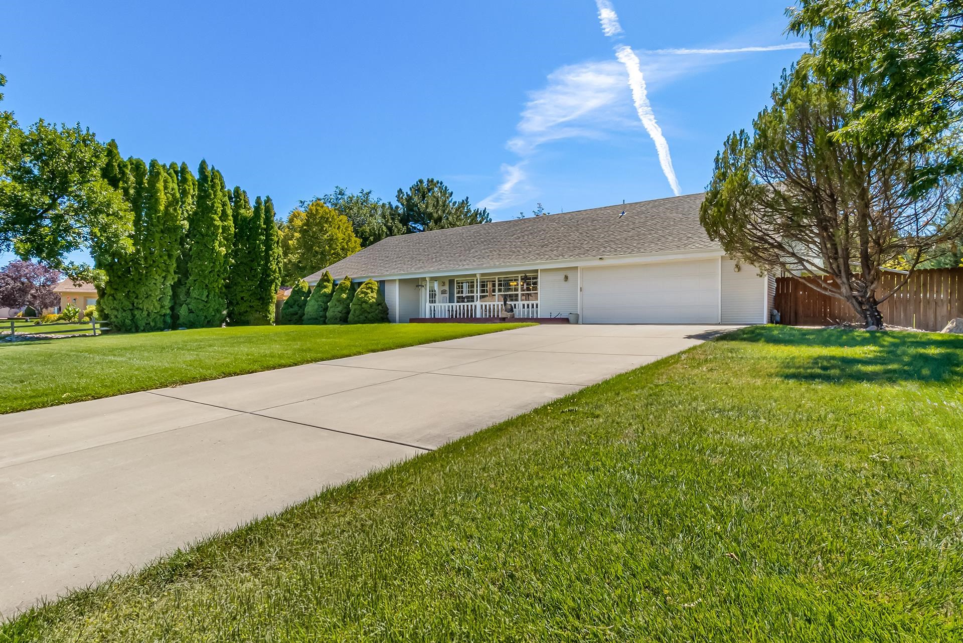 Single-story white home with an attached garage, covered porch, wide driveway, and landscaped lawn.