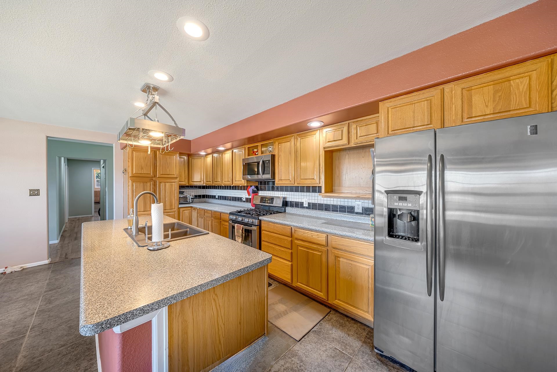 Kitchen with honey-colored cabinets, a speckled island sink, and stainless steel appliances.