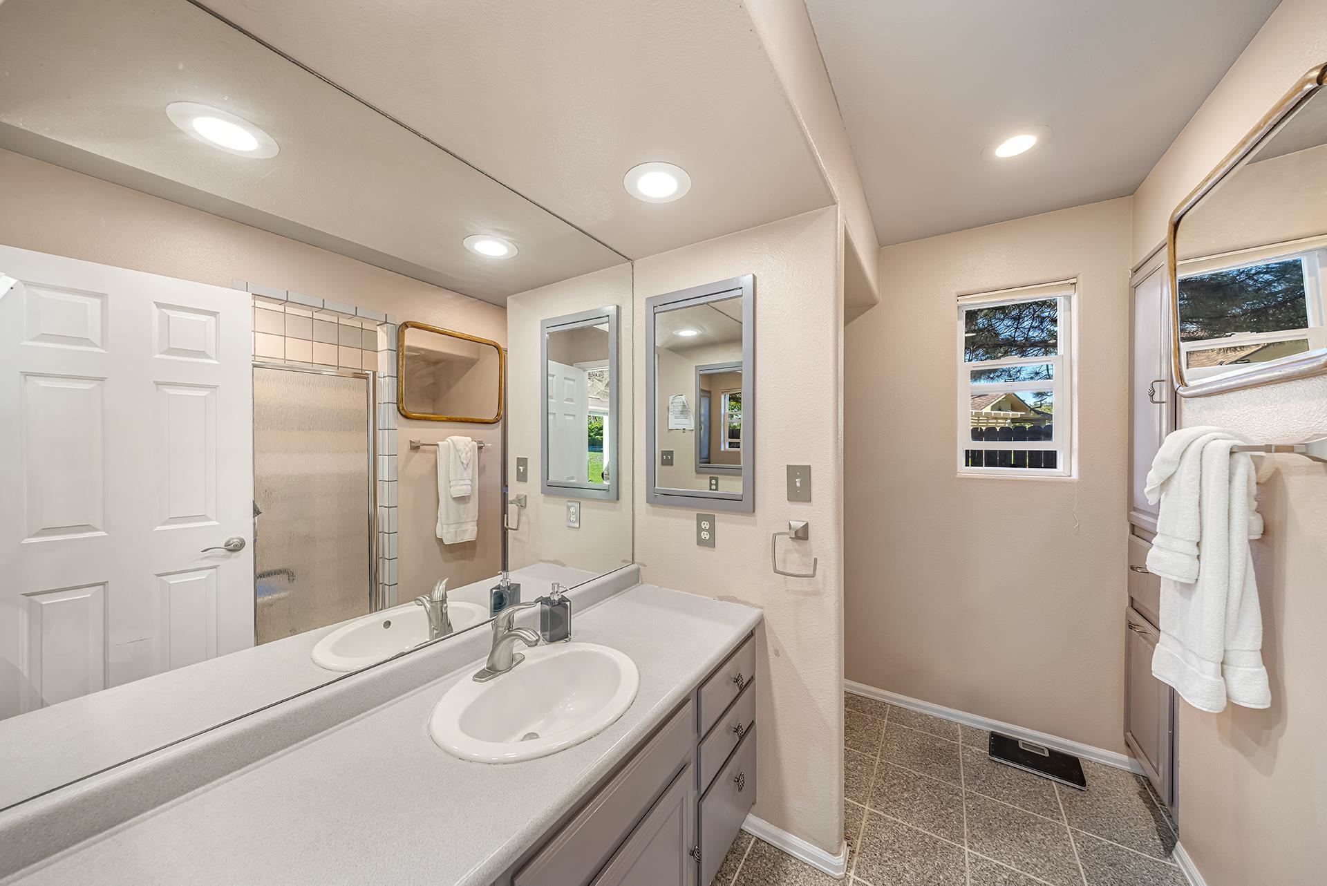 Bathroom with a double-sink vanity, large mirrors, and a frosted-glass shower door.
