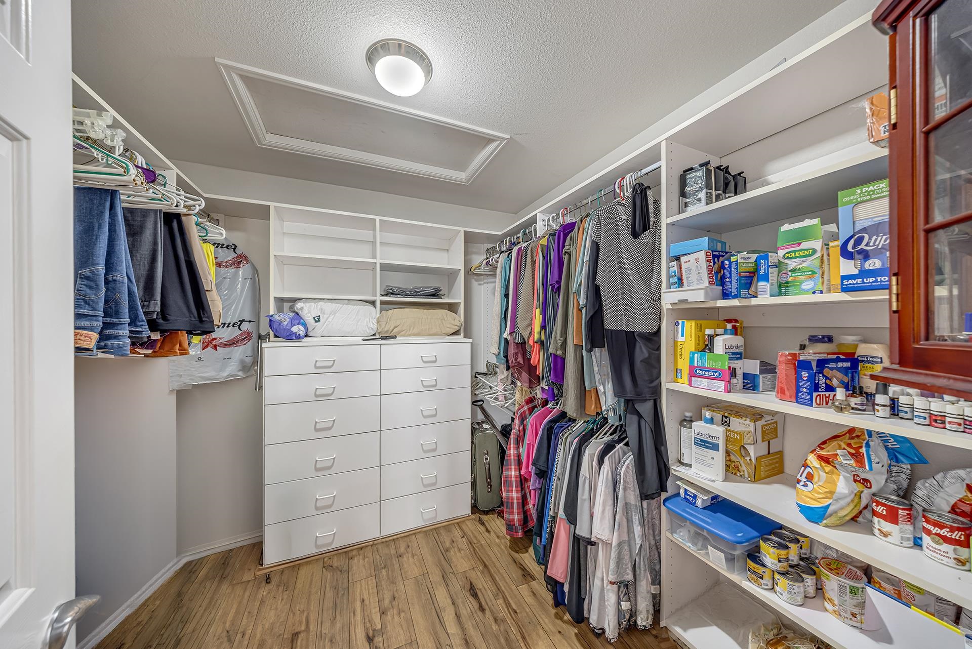 Walk-in closet with built-in drawers, hanging clothes, and shelves stocked with household supplies.
