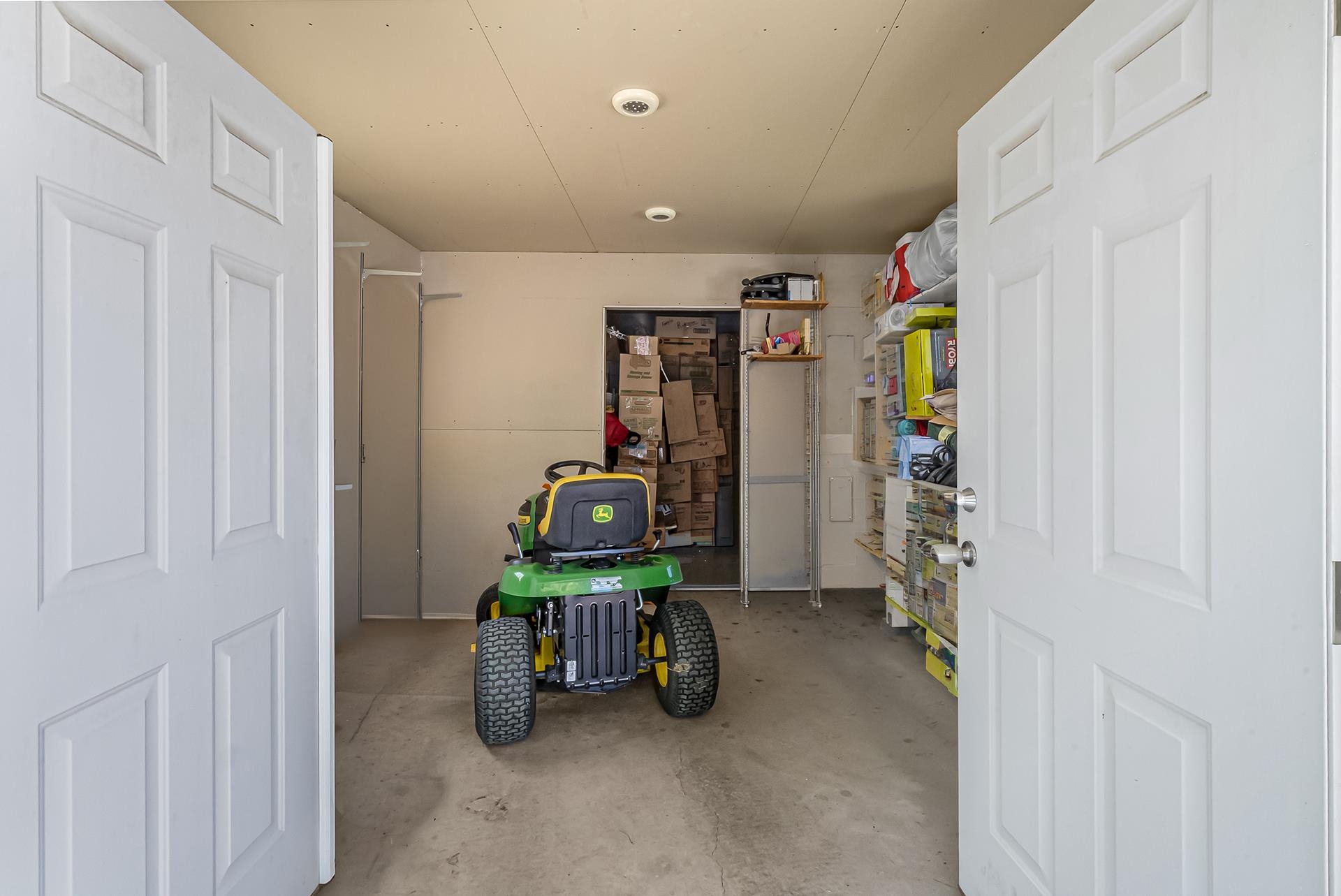 Garage with a green riding mower, storage shelves, and stacked boxes.