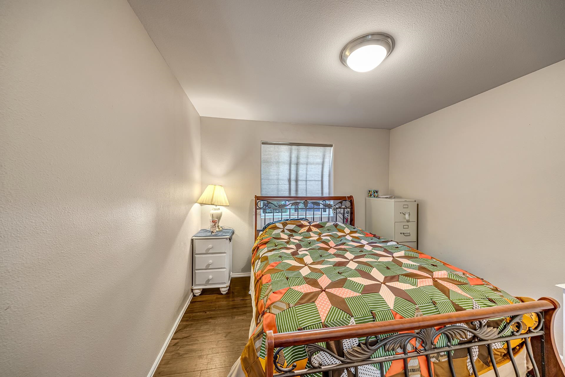 Bedroom with a metal bed and colorful patchwork quilt, beside a window with blinds.