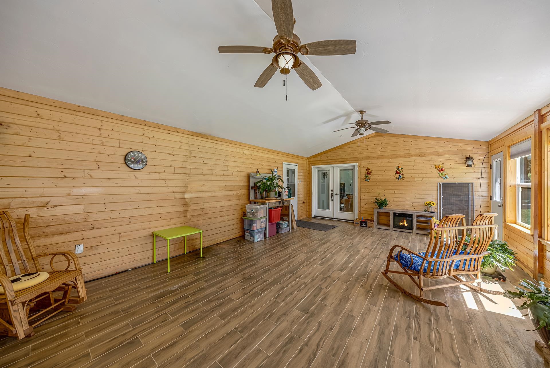 Wood-paneled sunroom with tile floors, patio chairs, and a small fireplace.