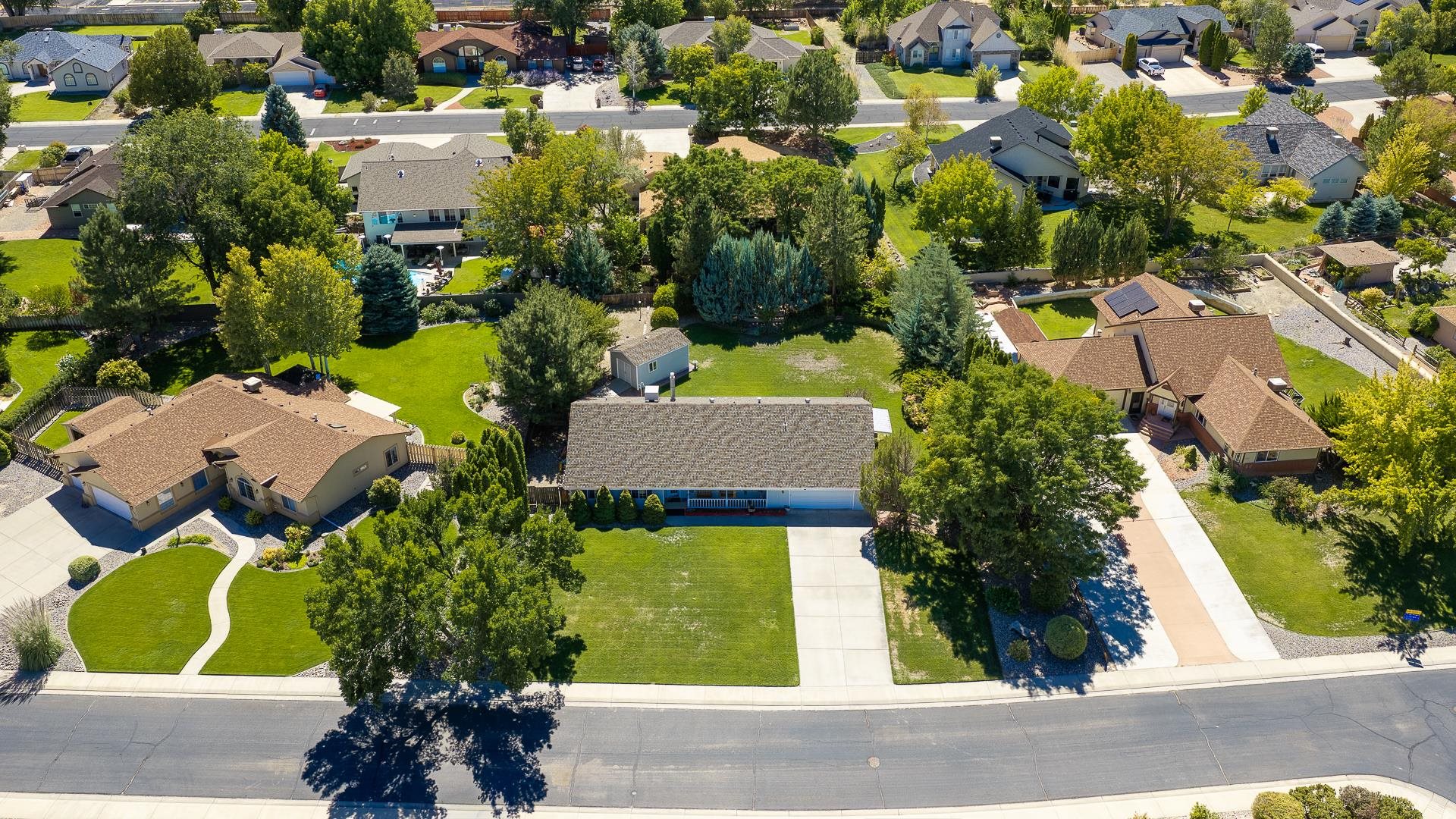 Aerial view of a single-story home with a broad lawn, mature trees, and detached shed.