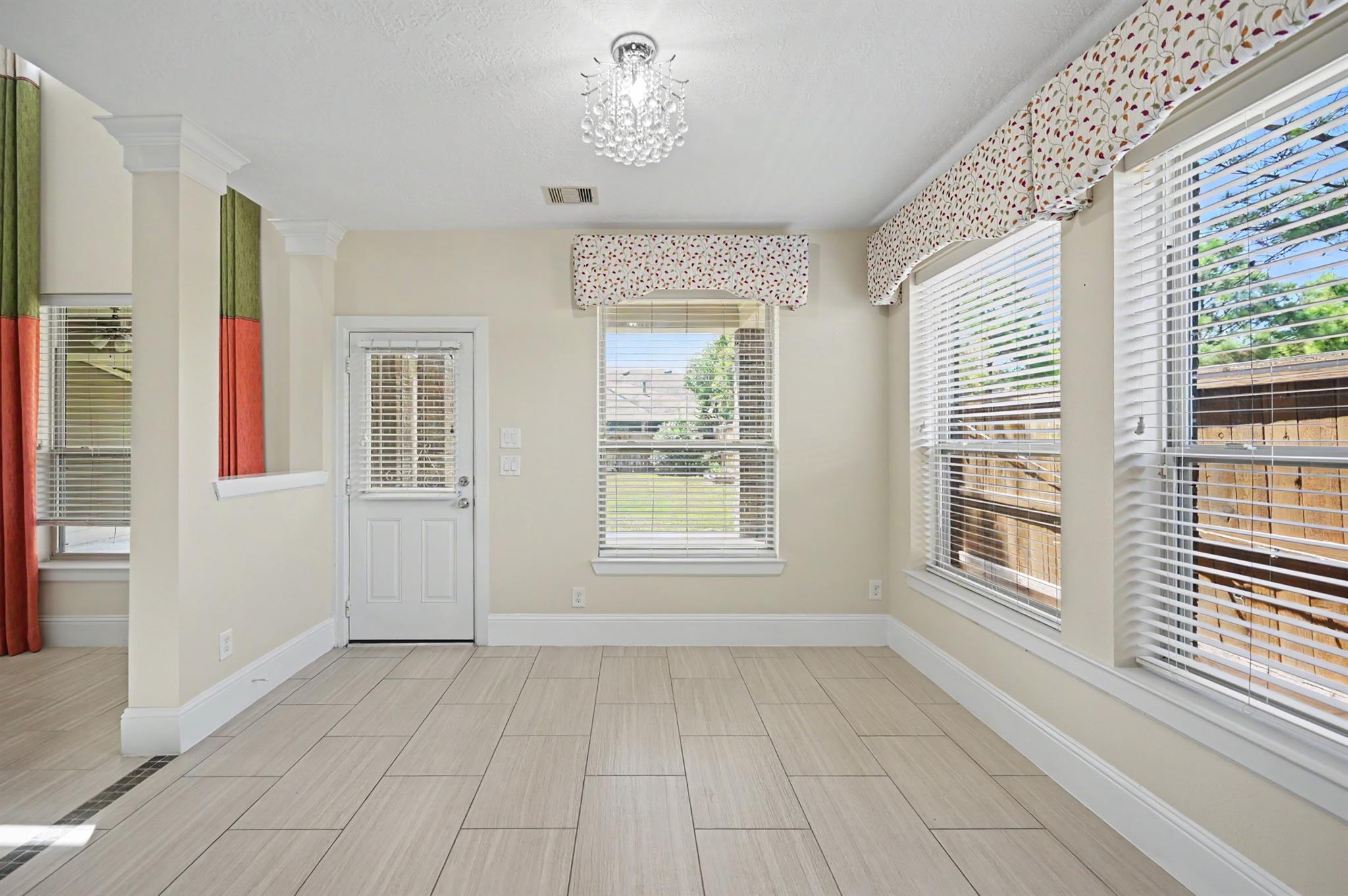 Bright tiled room with a chandelier, a door, and multiple windows with blinds.