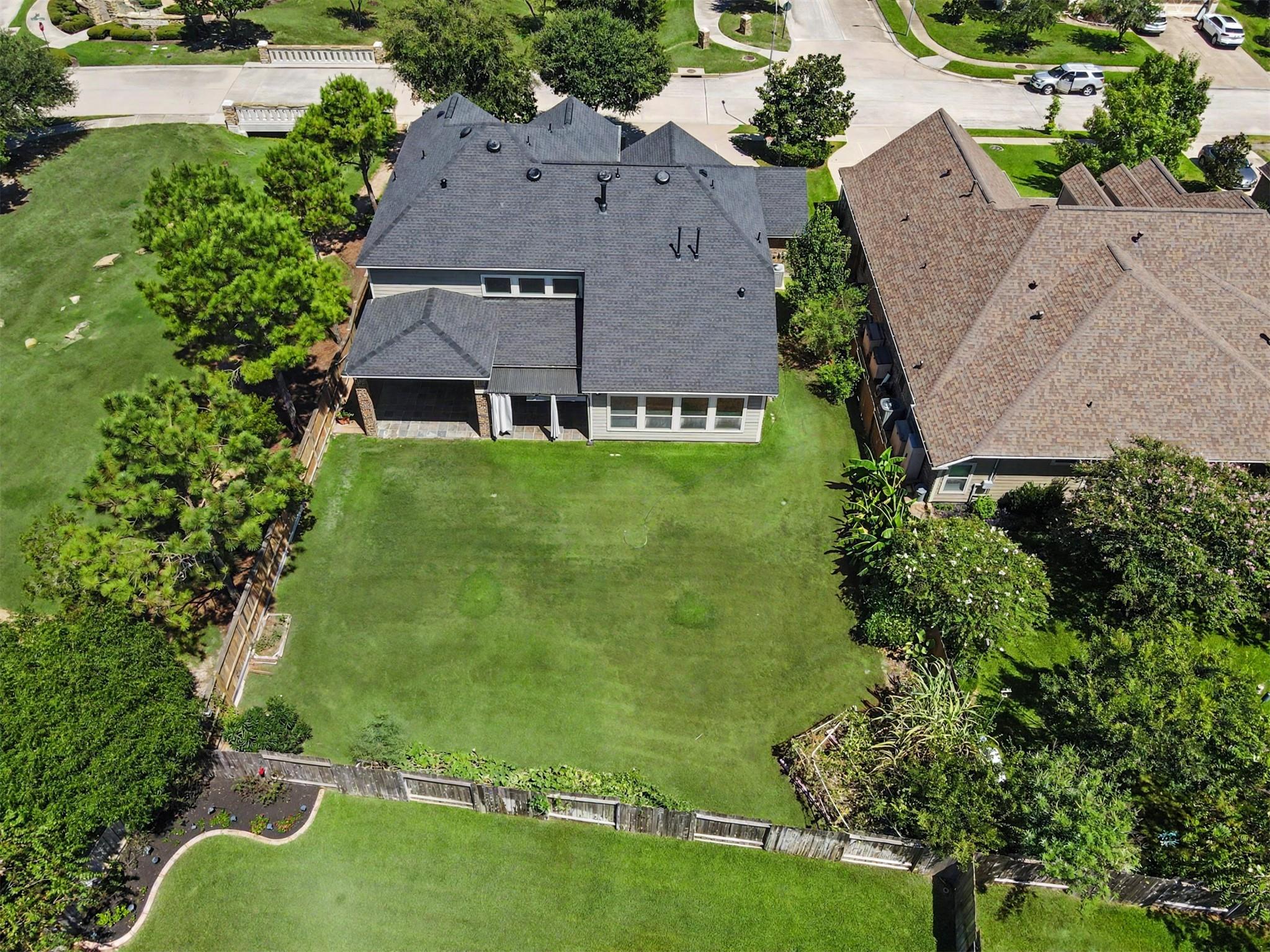 Aerial view of the home's rear, with a broad fenced lawn and covered patio.