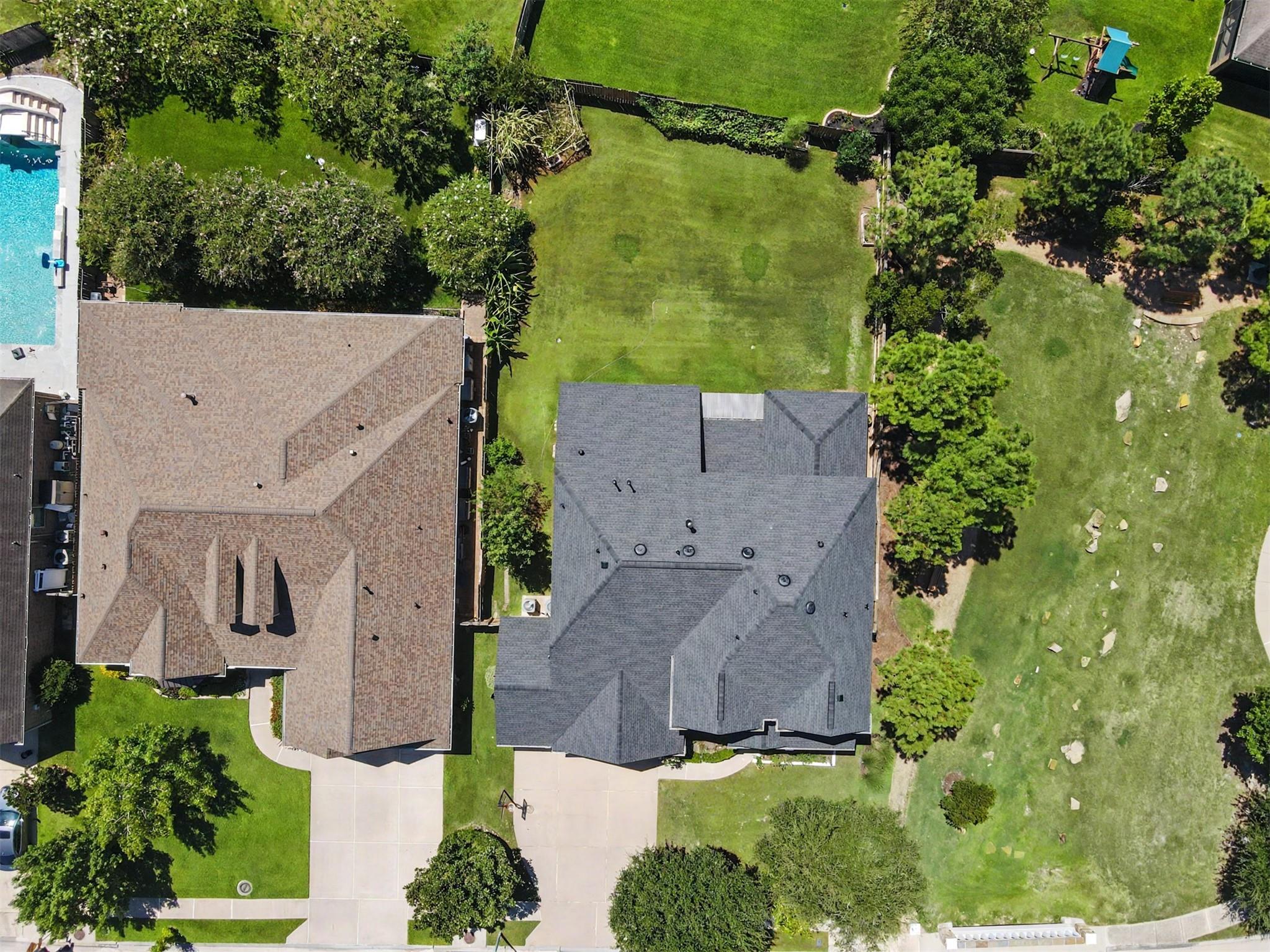 Aerial view of a home with a broad green lawn, driveway, and mature trees.