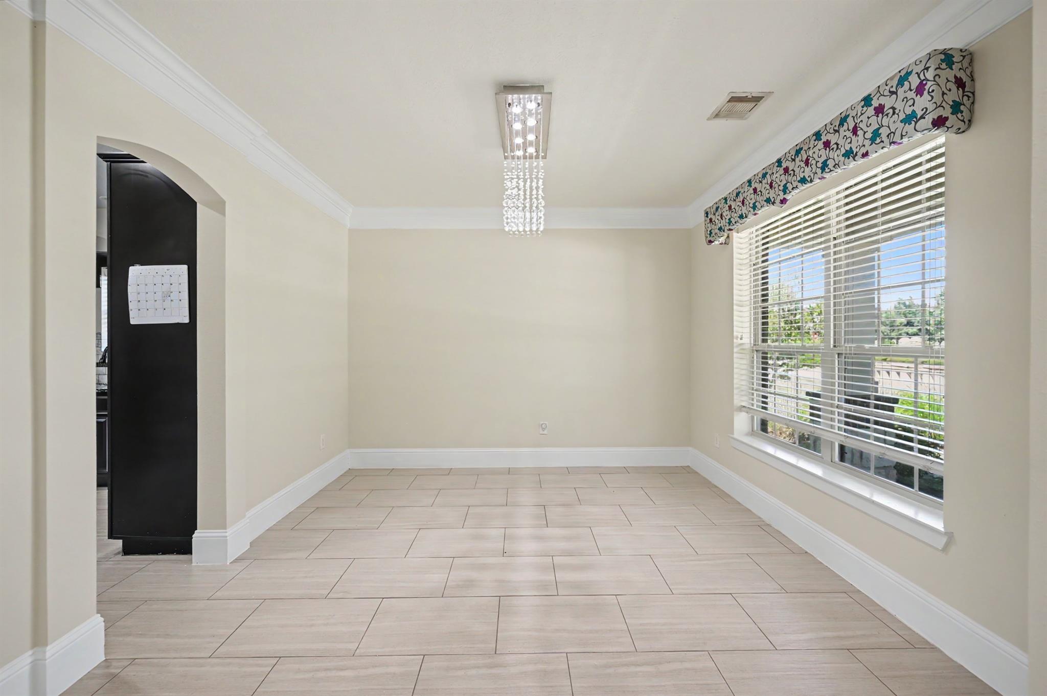 Empty dining room with a crystal chandelier, tiled floor, and large window with blinds.