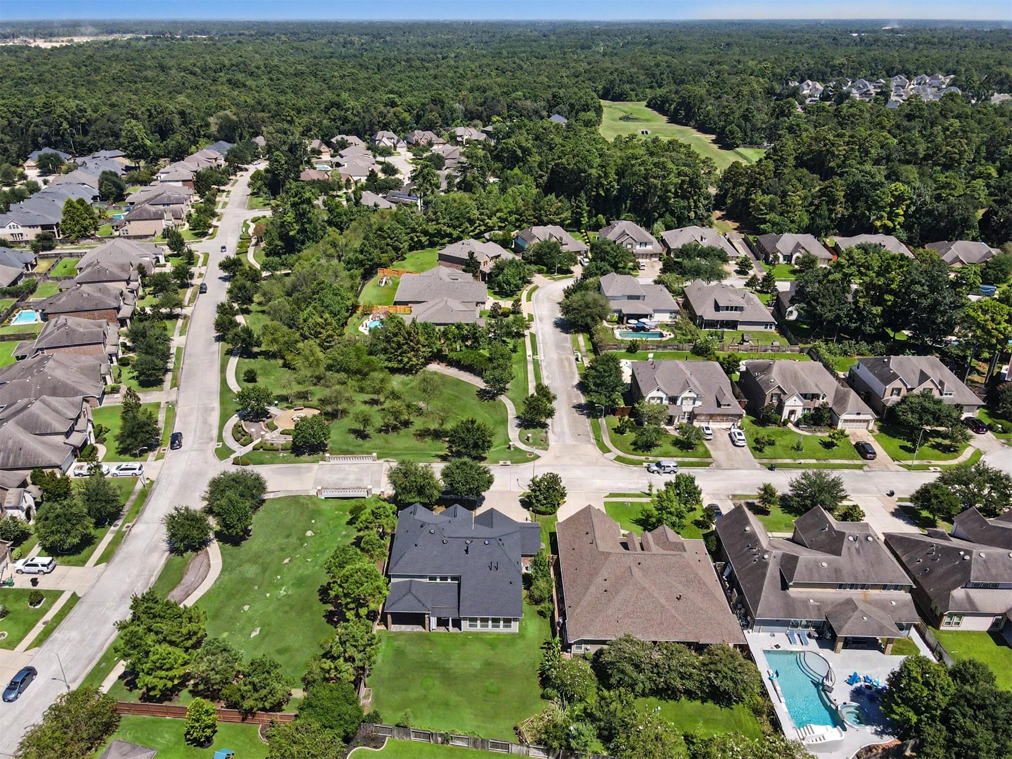 Aerial view of a home with a large lawn in a wooded residential neighborhood.