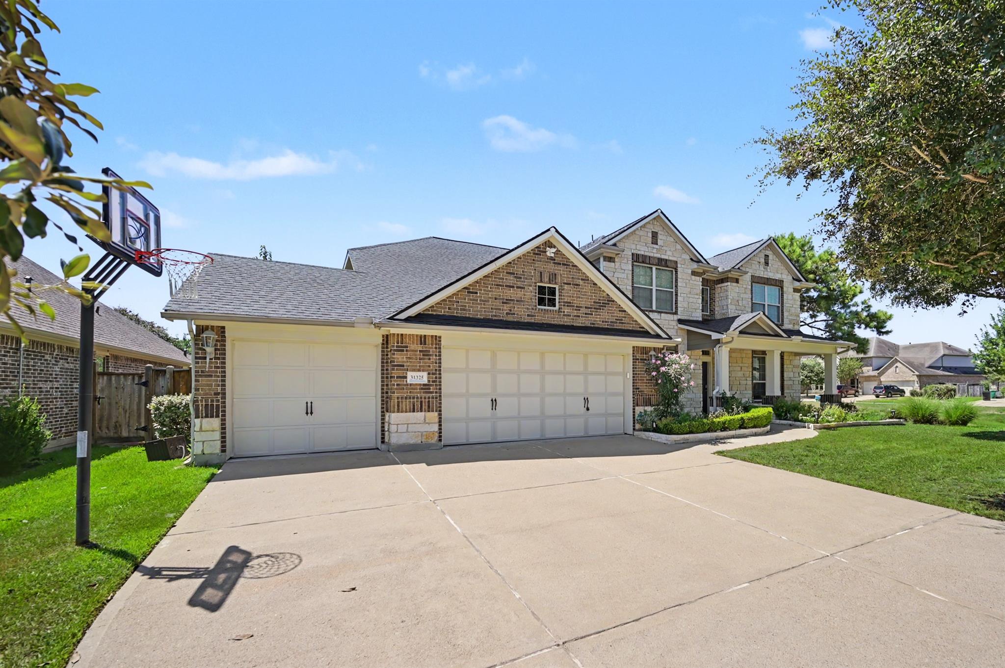 Two-story brick and stone house with a three-car garage and basketball hoop by the driveway.