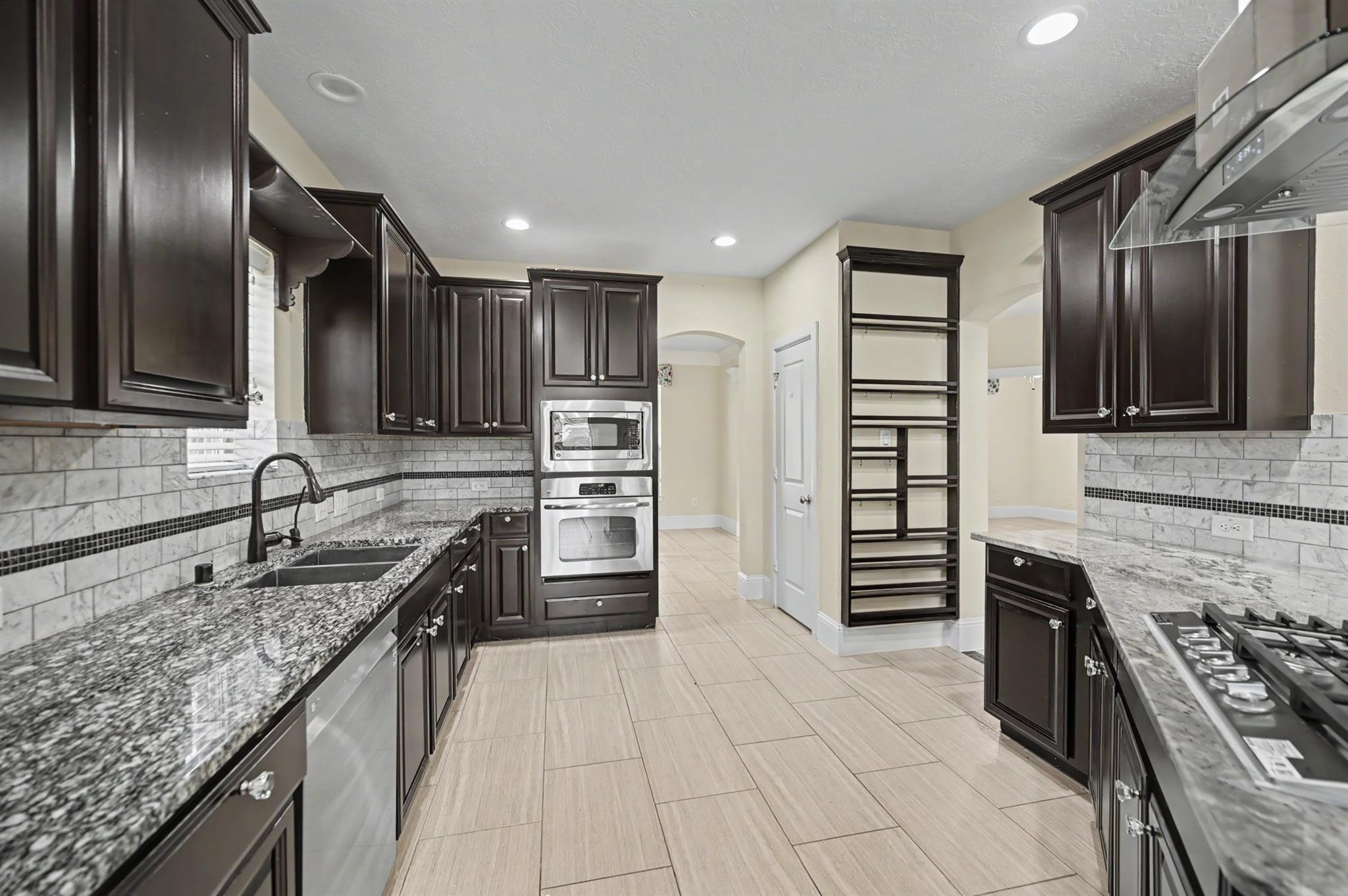 Kitchen with dark wood cabinets, granite counters, marble backsplash, and a built-in double oven.