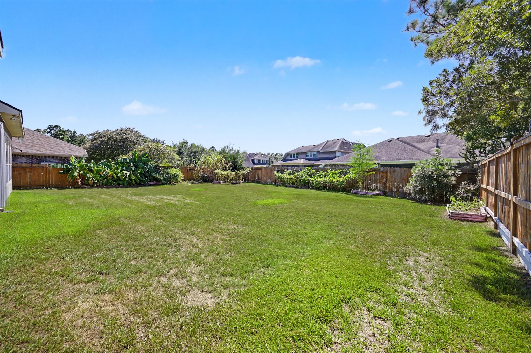 Spacious fenced backyard with a broad lawn, garden beds, and mature trees.