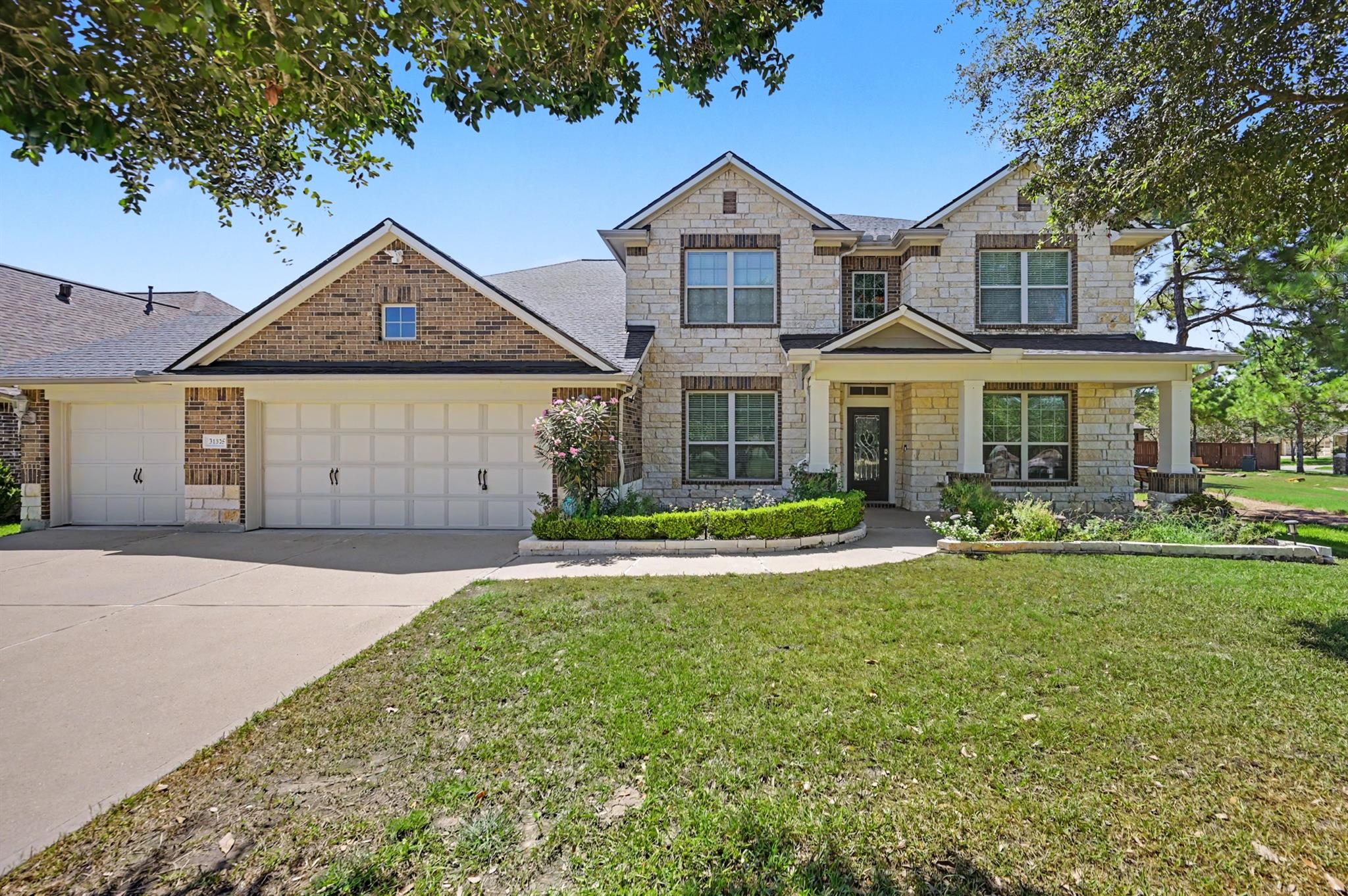 Two-story stone-and-brick home with a three-car garage, covered porch, and landscaped front yard.