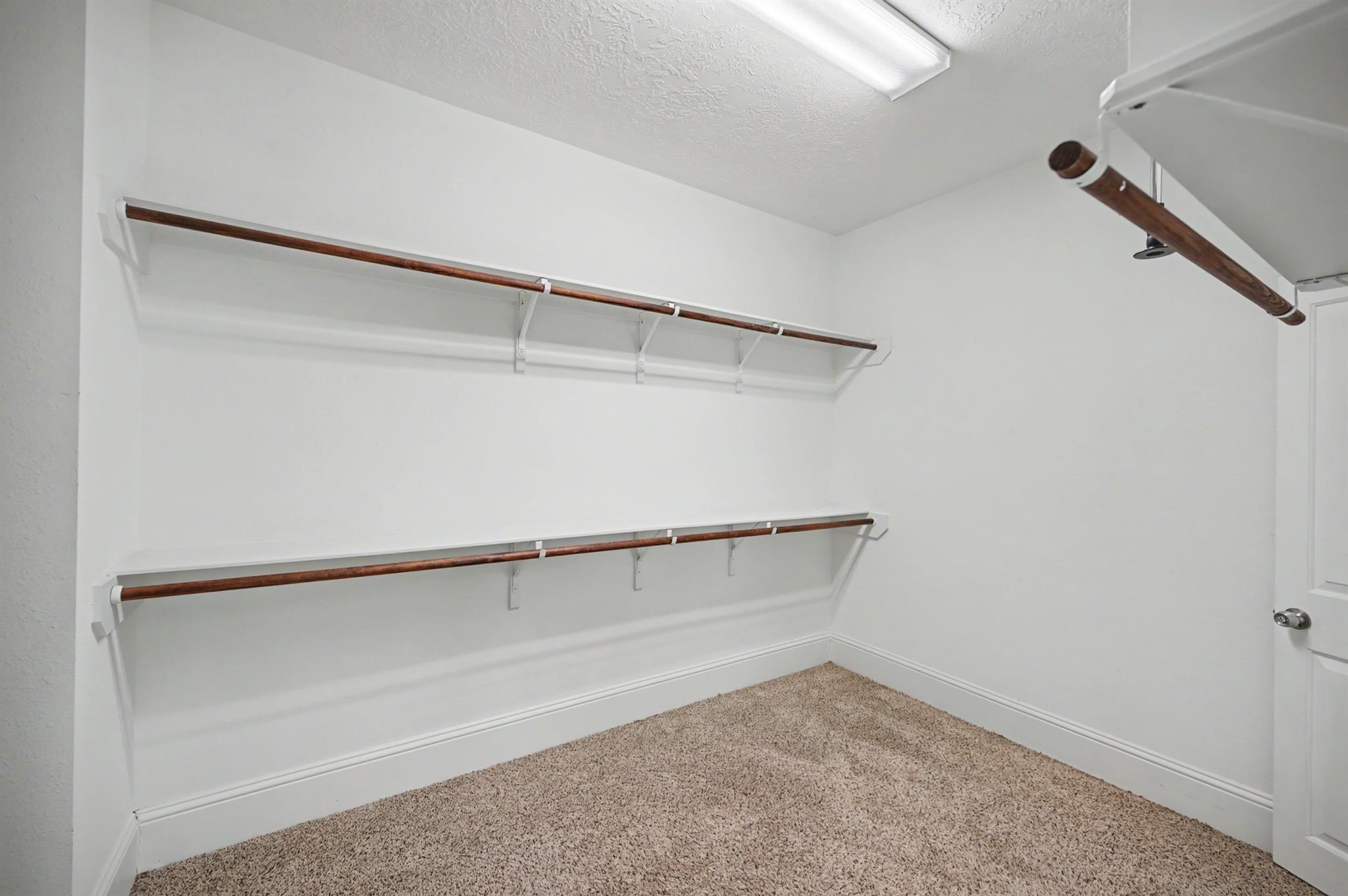 Empty closet with two levels of wooden hanging rods, shelves, and beige carpet.