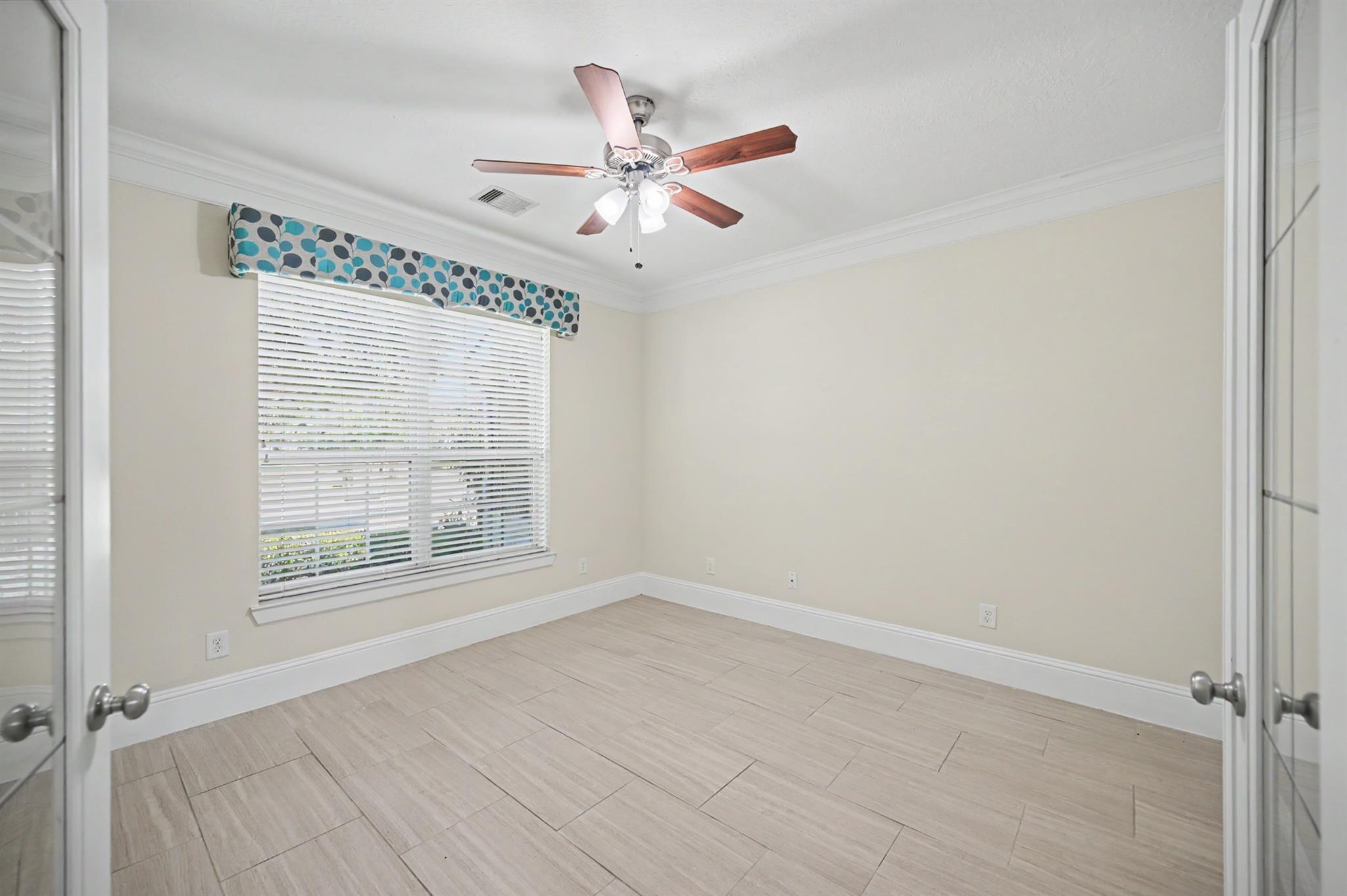 Empty room with light tile flooring, a window with blinds, and a ceiling fan.