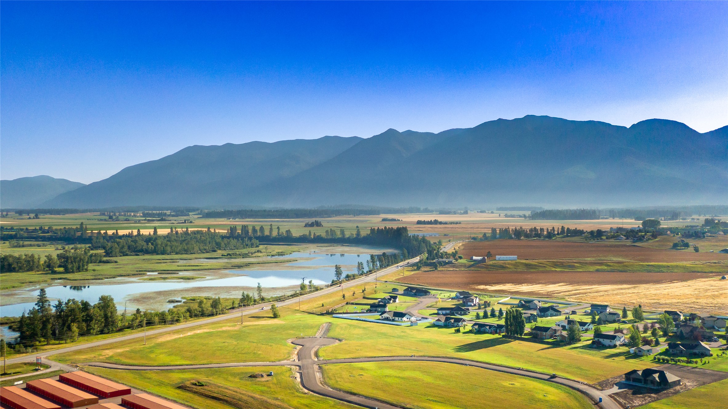Aerial view of a residential development, wetlands, farmland, and a mountain range.